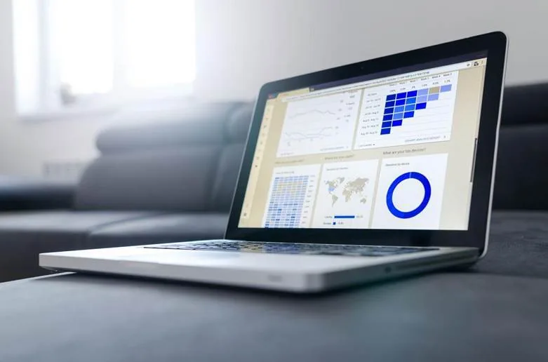 Laptop on a sofa showing an analytics dashboard with line charts, a cohort heatmap, a world map and a donut chart