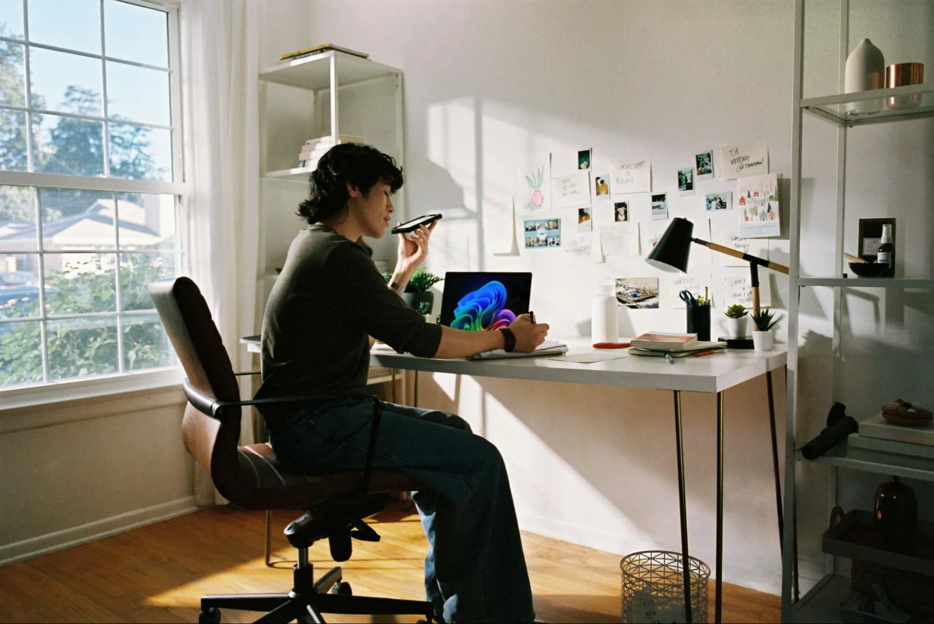 Person working at a desk with a laptop and phone in a sunlit home office