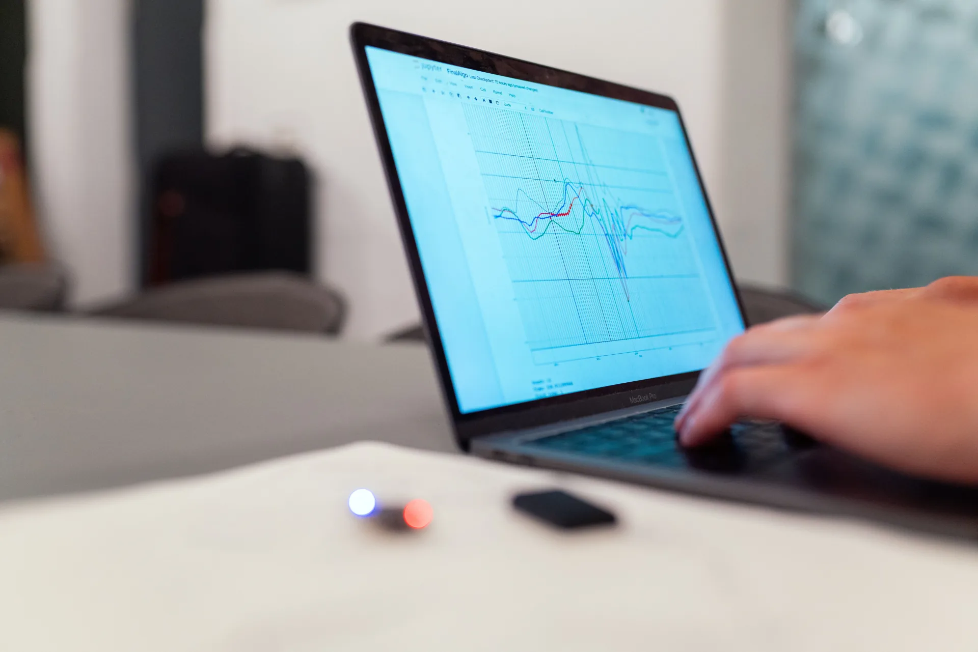 Close-up of a laptop screen showing a data analysis notebook with overlapping line charts, a hand resting on the trackpad